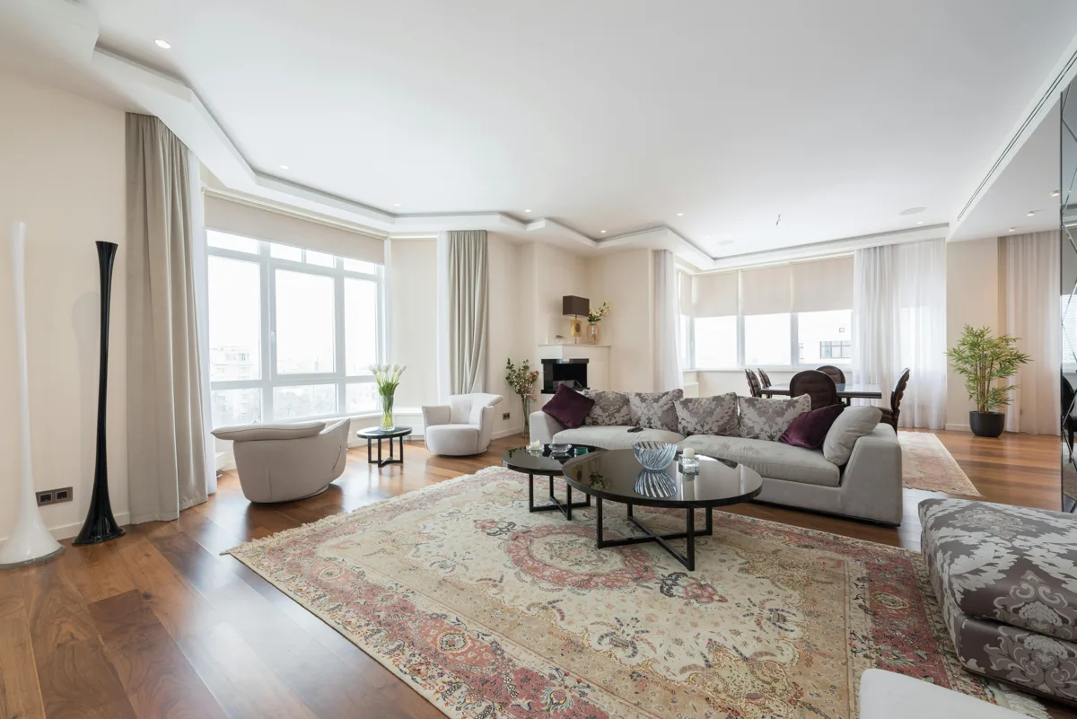 A light-filled living room with comfortable seating, a patterned rug, and warm wooden floors